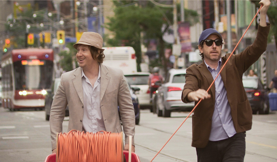 Two people laying orange cable on a city street with a Streetcar in the background.