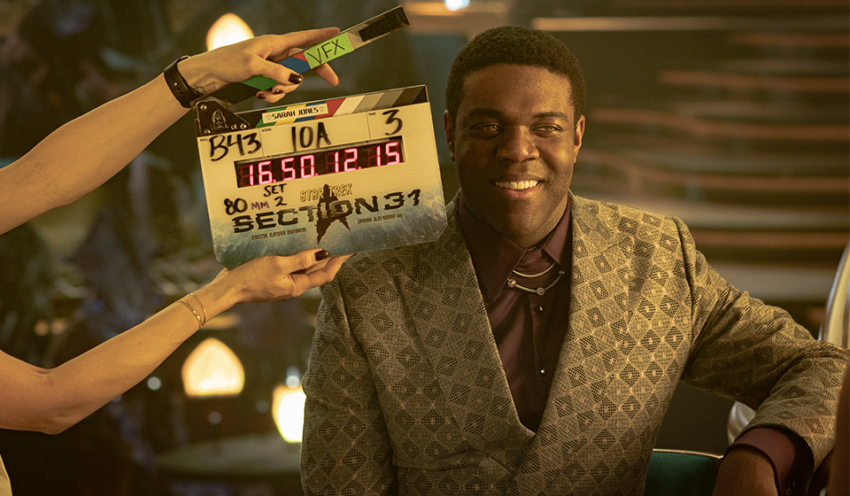 An actor ready standing next to a film shoot clapboard.