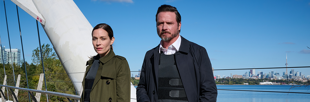 Two people standing on a bridge with the Toronto skyline in the background.
