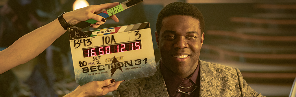 An actor ready standing next to a film shoot clapboard.