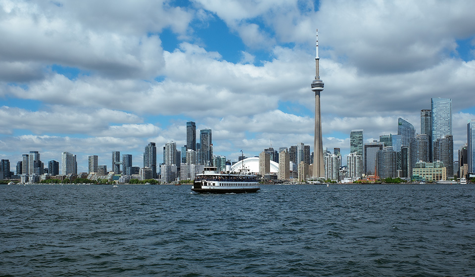 A ferry boat on the lake in Toronto's inner harbour with the downtown skyline in the background on a sunny day.