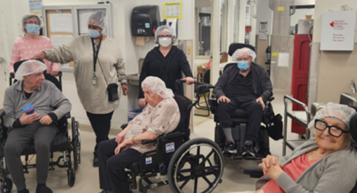 Seven staff and residents pose together for a group photo, with residents seated in wheelchairs and staff standing behind them in an indoor setting.