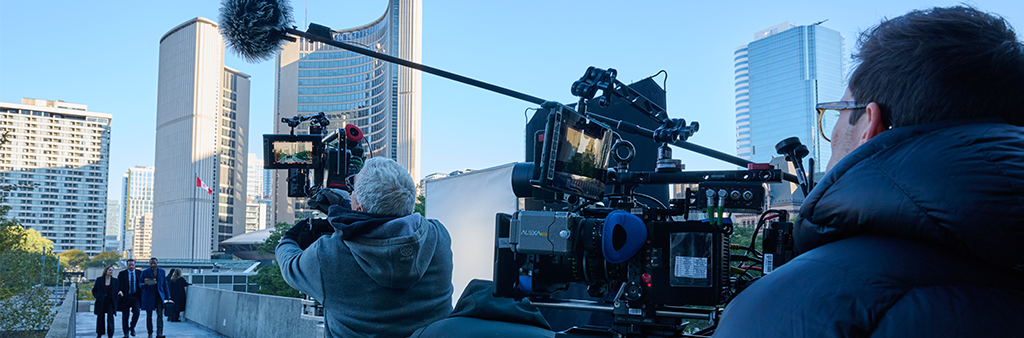 A film crew working with Toronto City Hall in the background.
