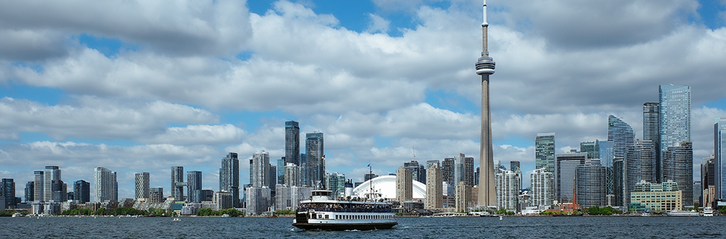 A ferry boat on the lake in Toronto's inner harbour with the downtown skyline in the background on a sunny day.