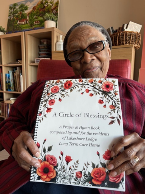 A resident smiles and holds up a copy of Circle of Blessings, a Lakeshore Lodge Prayer & Hymn Book.