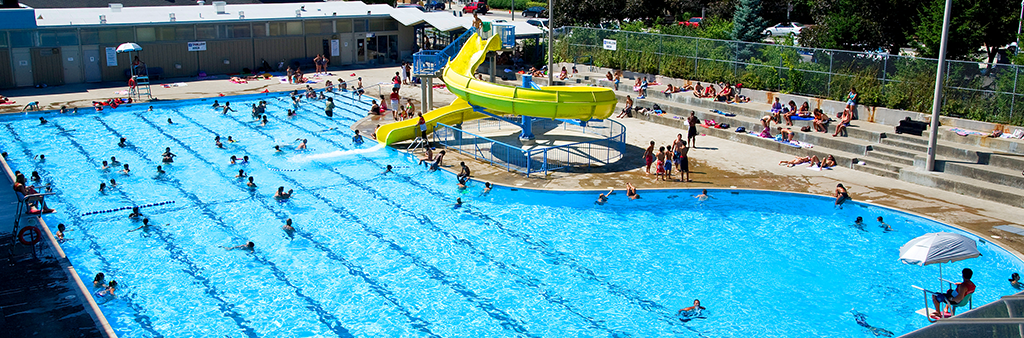 A large outdoor pool with a yellow slide on a sunny day.