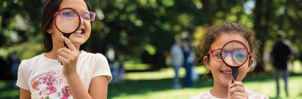 Two children look through magnifying glasses in an outdoor space