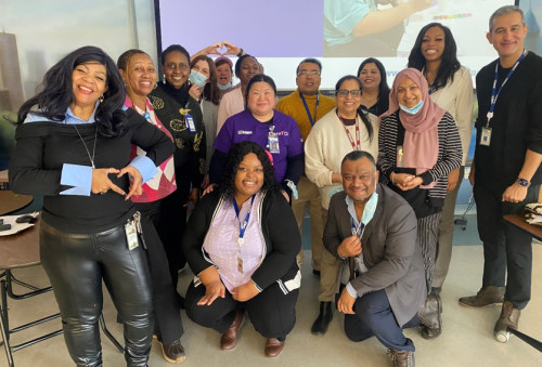 Fifteen staff members stand together for a group photo in a meeting room, gathered in front of a projector screen, reflecting teamwork and shared commitment to CareTO and improving long‑term care.
