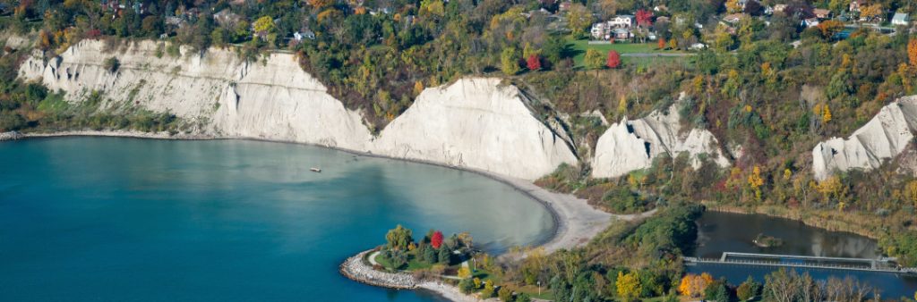 An aerial photo of Bluffer's Park looking north. The Bluffer's Park western beach and headland is visible in the foreground, the Scarborough Bluffs in the midground, and the vegetated tableland in the background.