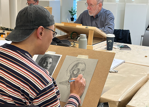 Person draws portrait on easel in a classroom