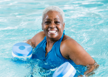 Senior woman wearing a blue bathing suit floating on a pool noodle in a pool.