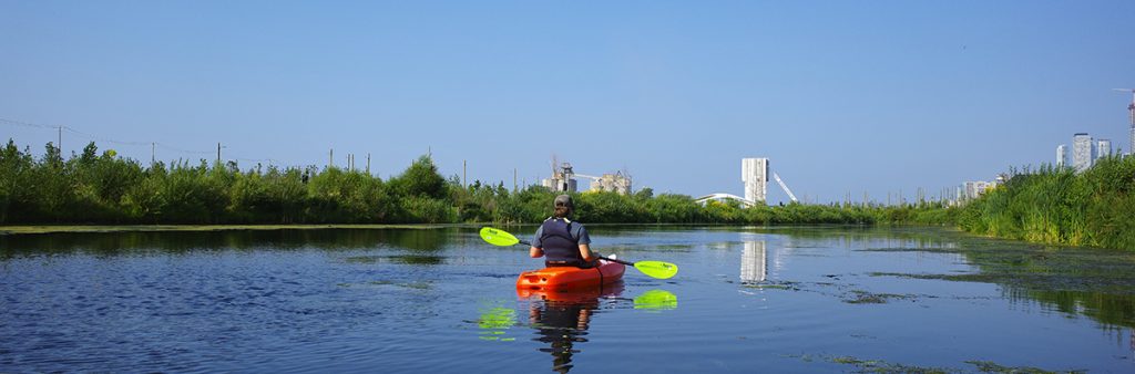 A single kayaker at Biidaasige Park, on a bright sunny day.