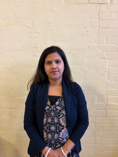Headshot photograph of a women with long black hair wearing pattern blouse and black blazer