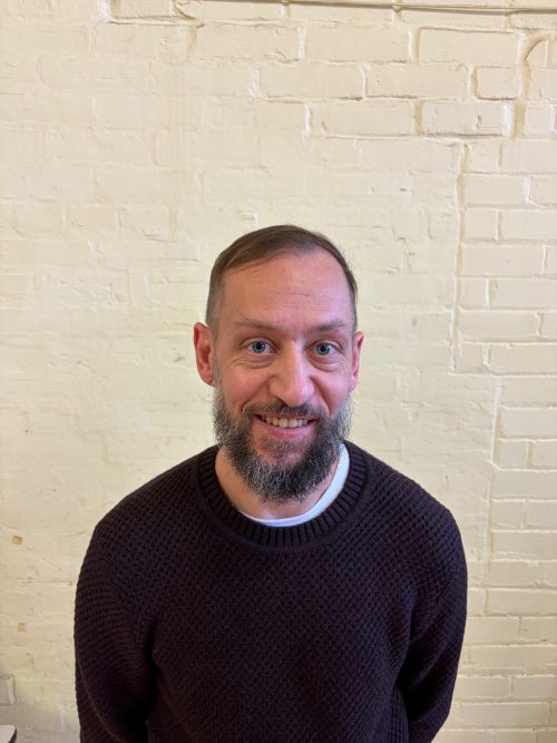 Headshot photograph of a man wearing black sweater