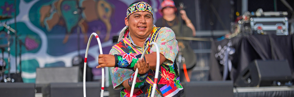 Close up of a hoop dancer with a stage and cellist in the background