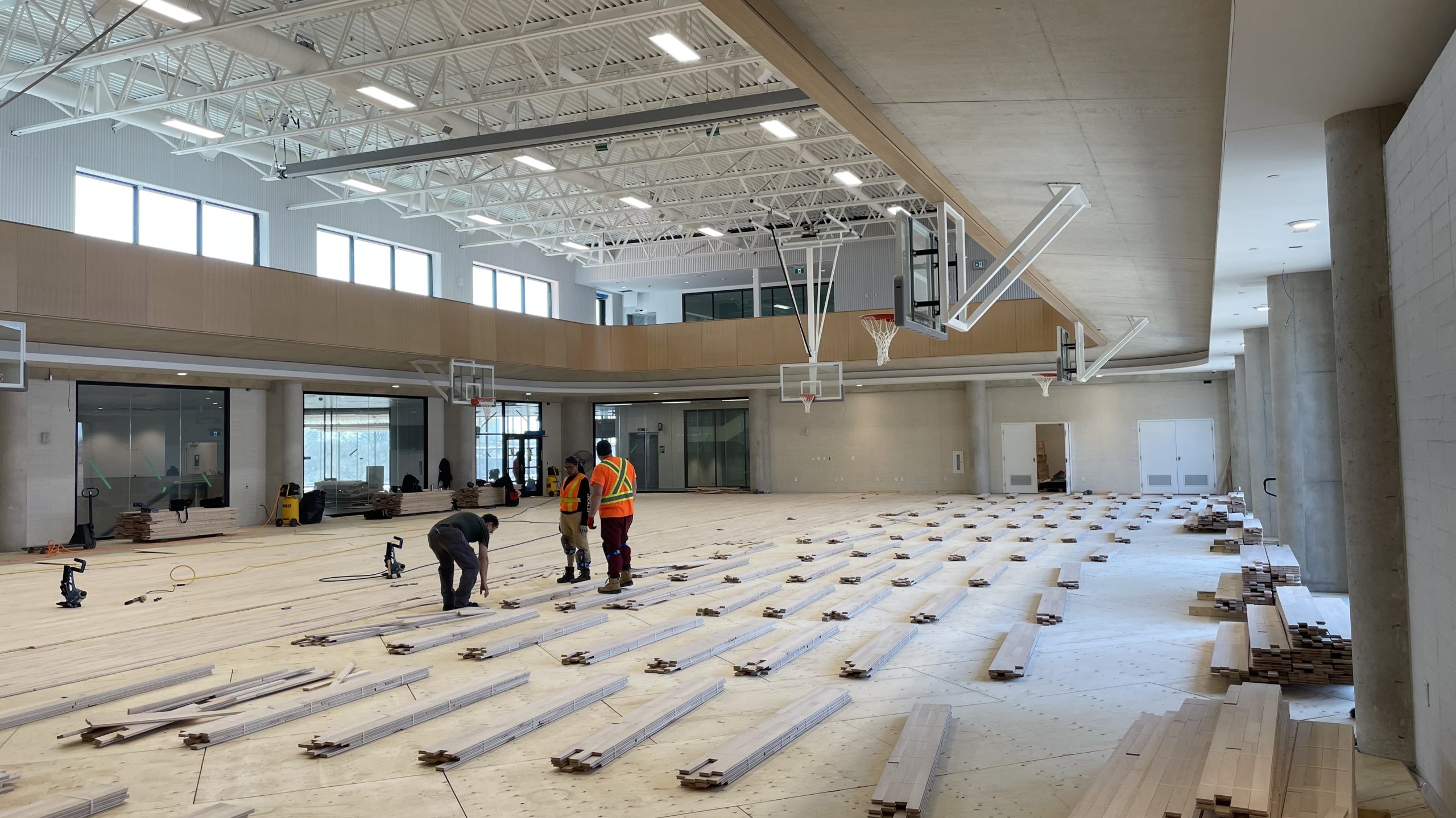 A photograph showing workers in the gym laying out wood flooring for installation.