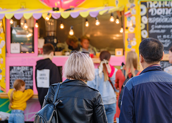 Two people standing in front of food vendor with lights and a colourful facade.