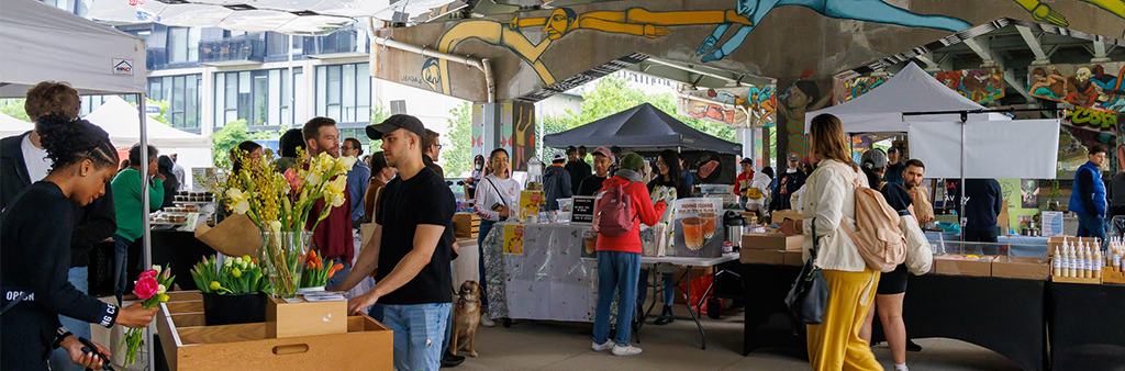 People shopping at an outdoor market set under an underpass.