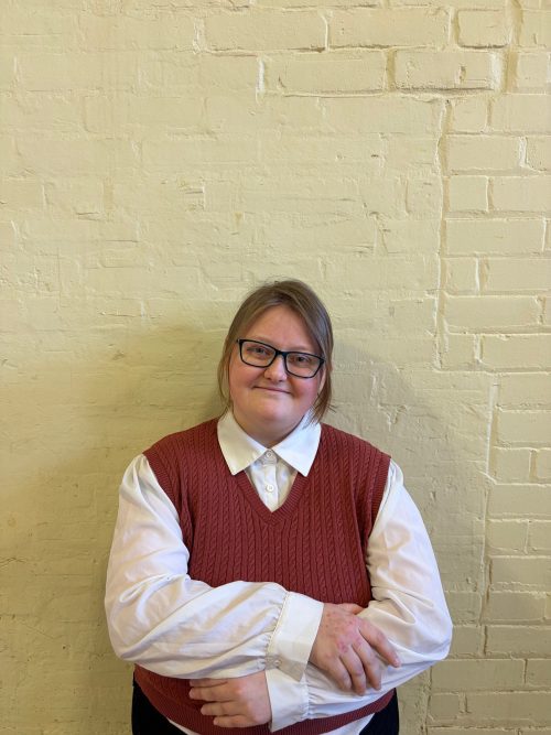 Headshot photograph of woman with glasses wearing white button shirt with red sweater vest