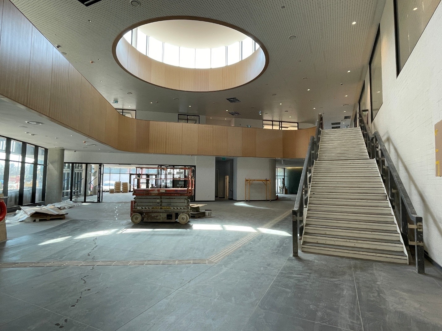 Photograph of the atrium under construction at the Wallace Emerson Community Recreation Centre. The large open area has large tiled floors, and a wide stairway leading to a second floor area. A circular clerestory window feature is located above the second storey ceiling.