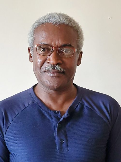Headshot photograph of man wearing glasses and blue henley's shirt