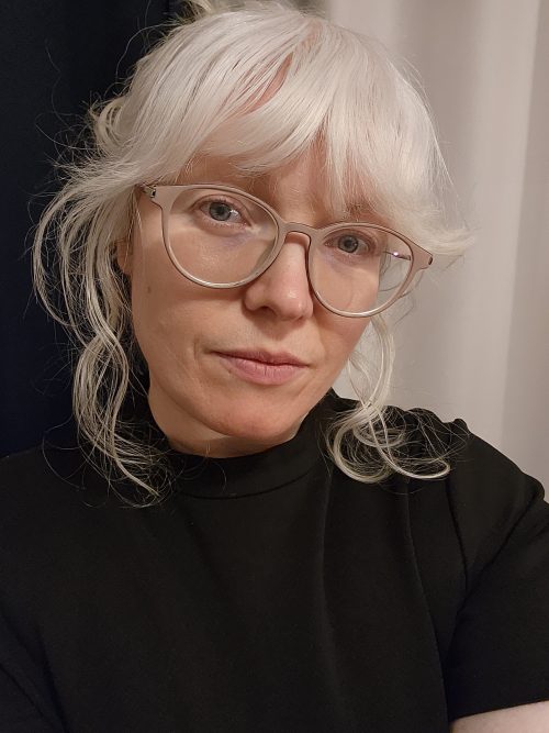 Headshot photograph of woman with light blonde to white hair wearing glasses