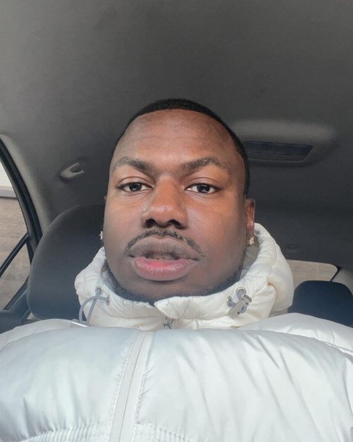 Headshot photograph of man wearing white jacket with hood. 