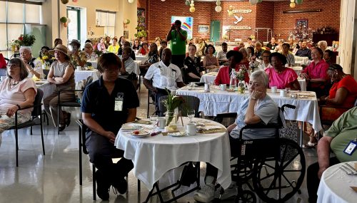 Residents and guests seated at decorated tables in a large hall during appreciation event.