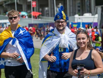 Three audience members wearing Bosnia Herzegovina flags, jersey, hat and tank top