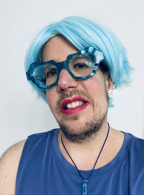 Headshot photograph of a person with blue hair and blue glasses