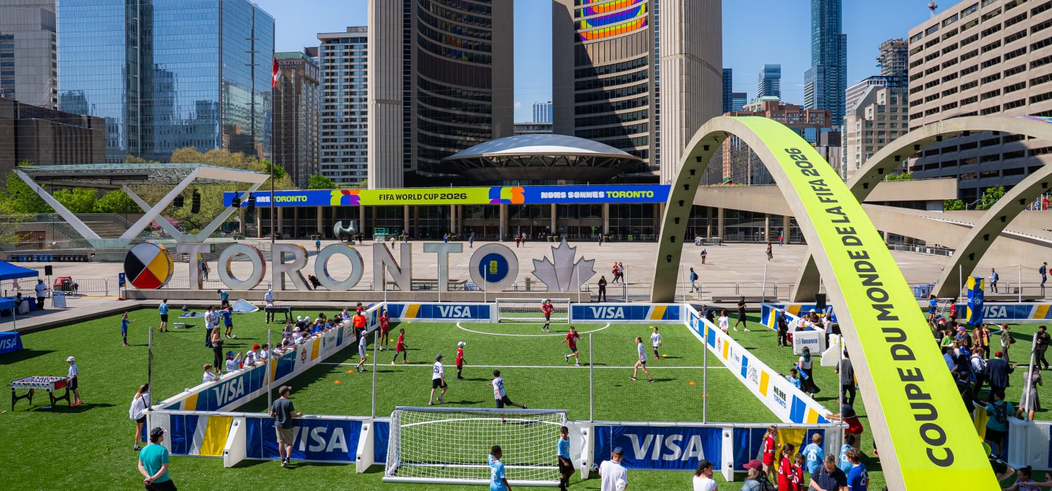 A temporary soccer pitch set up inside the fountain area of Nathan Phillips Square at Toronto City Hall. The square, TORONTO sign and City Hall are decorated with FIFA World Cup branding.