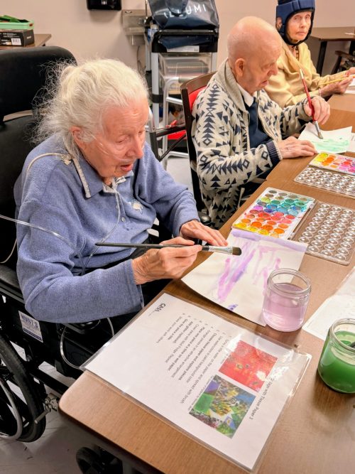 Residents seated at a table painting with watercolours, using brushes and paint palettes during an art activity.