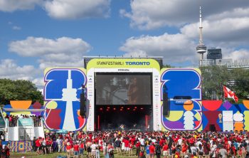 Stage with screen showing singer, audience watches, and CN Tower and buildings in the background