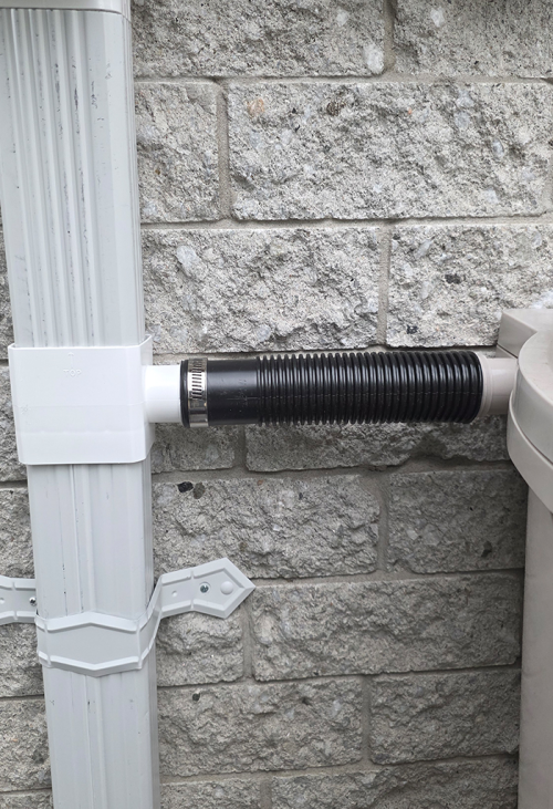 Downspout with diverter connecting to rain barrel against a background of grey brick