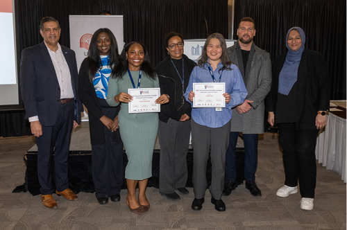 A group of seven people standing together and smiling, with two individuals holding certificates during an award presentation.