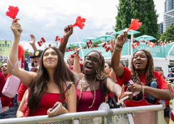 People behind a barricade wave maple leaf-shaped clappers and wear Canadian flag headbands.