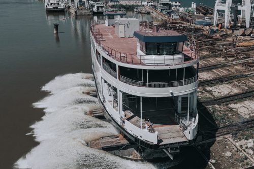 A partially constructed ferry boat being launched into the water.