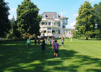 Children run across lawn towards historic house