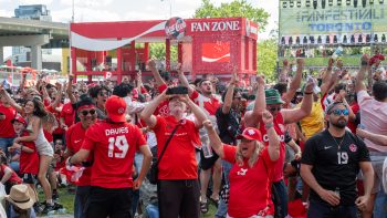Soccer fans cheer outside. Coca-Cola Fan Zone booth and FIFA Fan Festival Toronto banner in the background