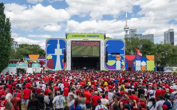 Stage with screen showing soccer match, audience watches, and CN Tower and buildings in the background