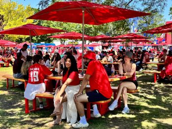fans enjoying themselves at FIFA Fan Festival, sitting on picnic tables with red umbrellas