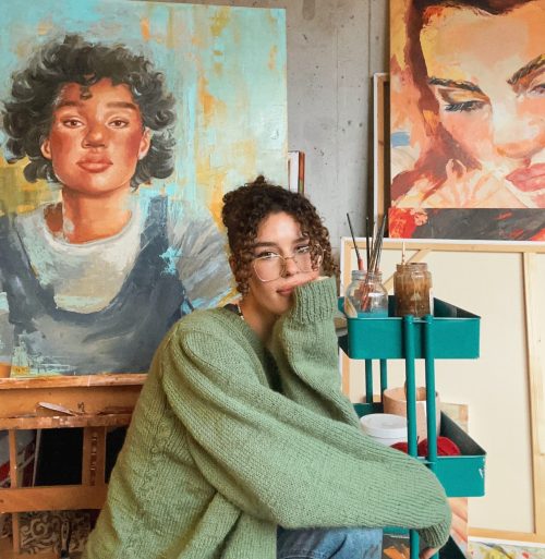 A person sitting in front of paintings on easels in a studio