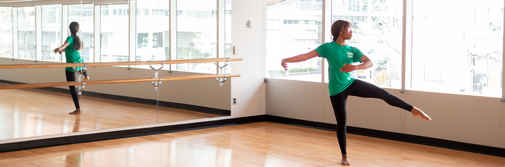 Person practicing a ballet pose in a bright dance studio with mirrored walls.