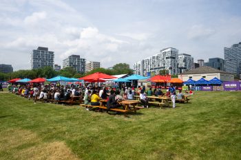 People seated at picnic tables with umbrellas in front of historic buildings and condos