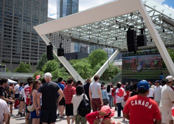 People watching soccer on a large outdoor screen in a public square.