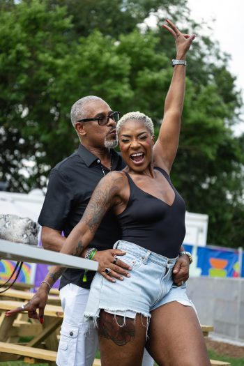 Jully Black smiles and raises hand in a peace symbol. Behind her is a person holding her waist and kissing her head.