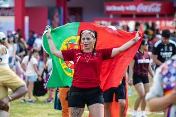 Person wearing a Portugal soccer jersey and head band holds up a Portugal flag behind them. Crowd and festival grounds in the background.