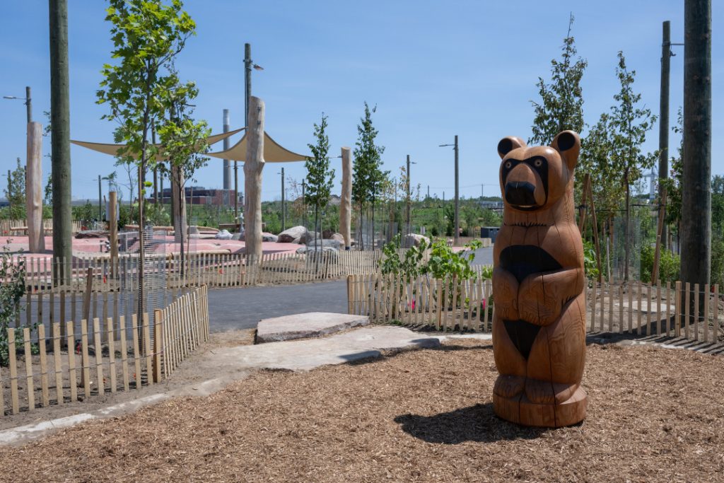 A bear art structure surrounded by fencing, trees and a blue sky.