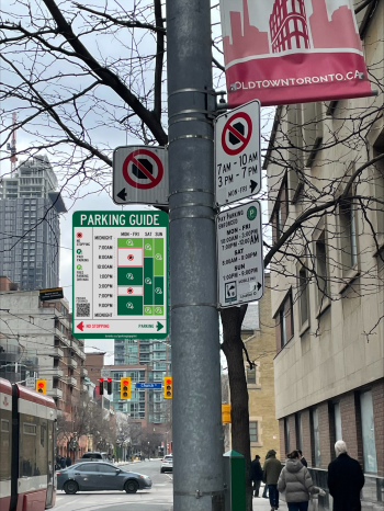 Street view showing a parking sign installation with a new Parking Guide sign mounted below existing parking regulation signs on a utility pole. The guide summarizes when no stopping, paid parking, and free 3-hour parking apply at the location.