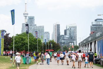 Crowds walk on paved path through festival grounds.